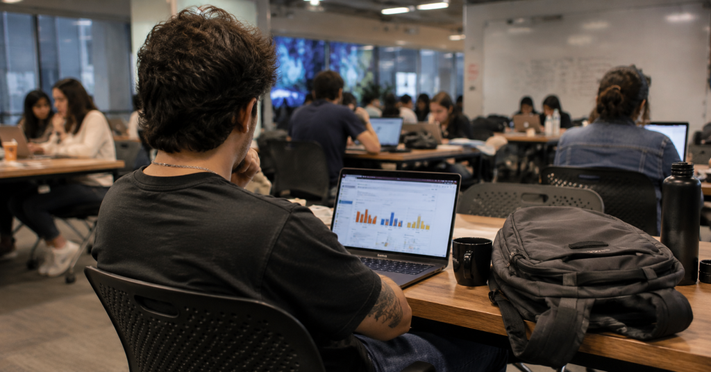Persona de espaldas revisando ofertas de empleo en una laptop dentro de un espacio de coworking, representando el ranking de desempleo en Latinoamérica 2026